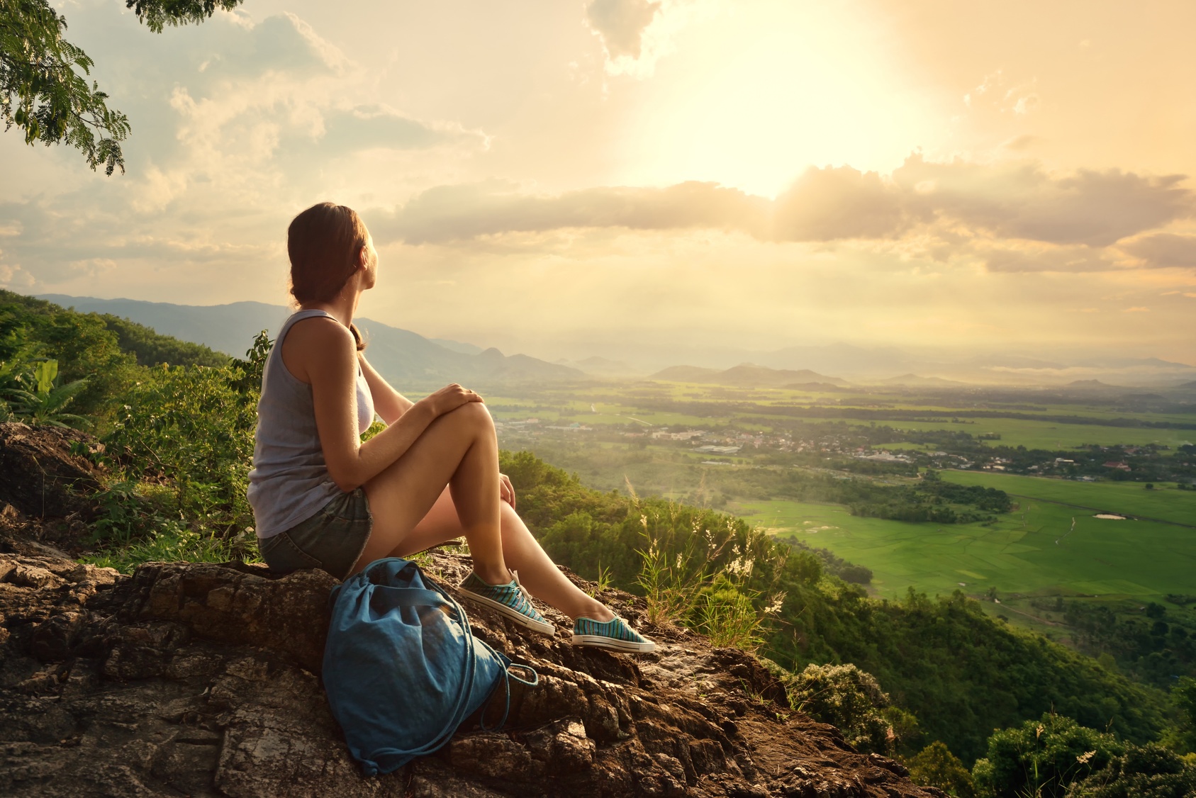 A girl sits on the edge of the cliff and looking at the sun valley and mountains