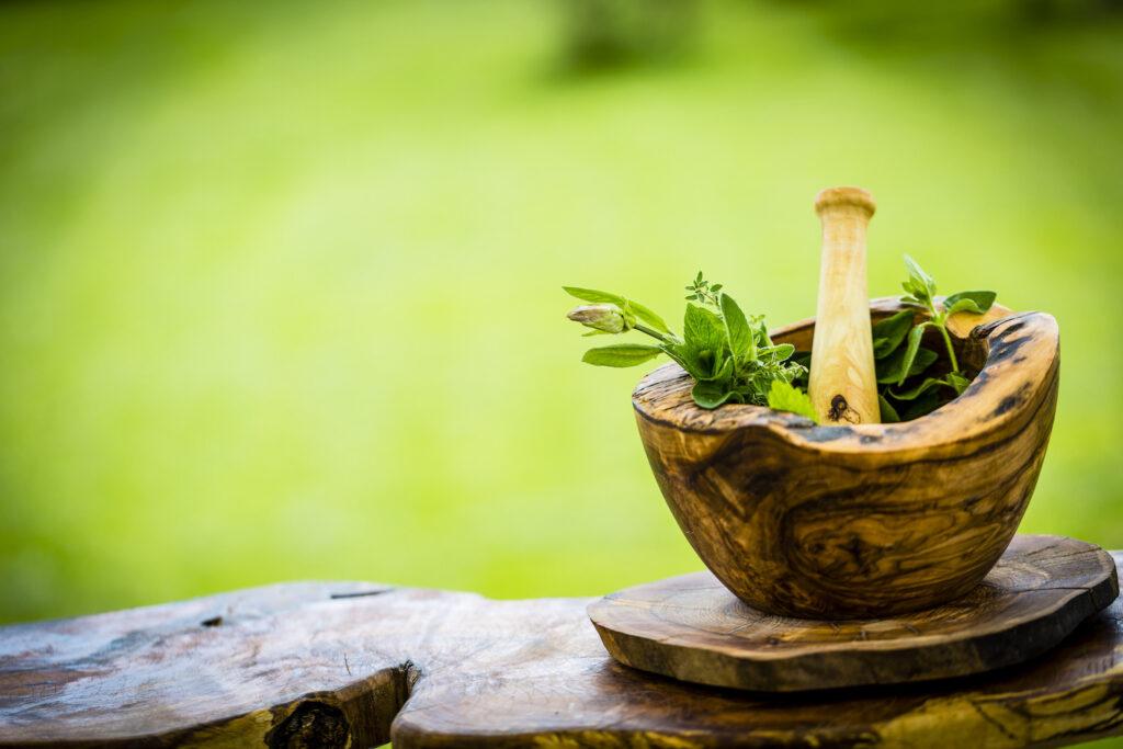 Fresh herbs from the garden in wooden olive mortar against with sunny garden background